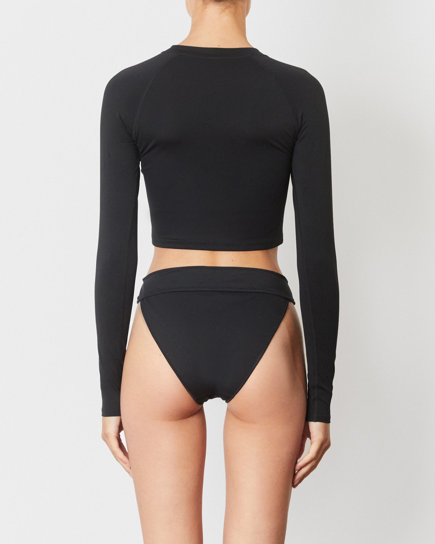 Studio image of model wearing the Contour Rashguard in Black, featuring its cropped body and full length sleeves. 