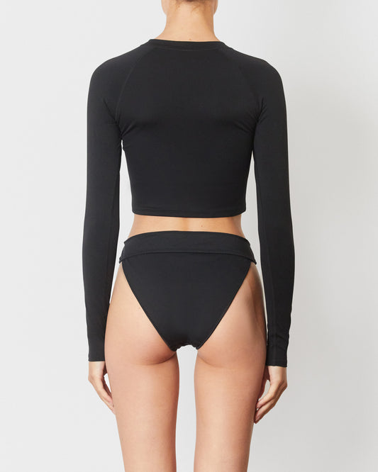 Studio image of model wearing the Contour Rashguard in Black, featuring its cropped body and full length sleeves. 